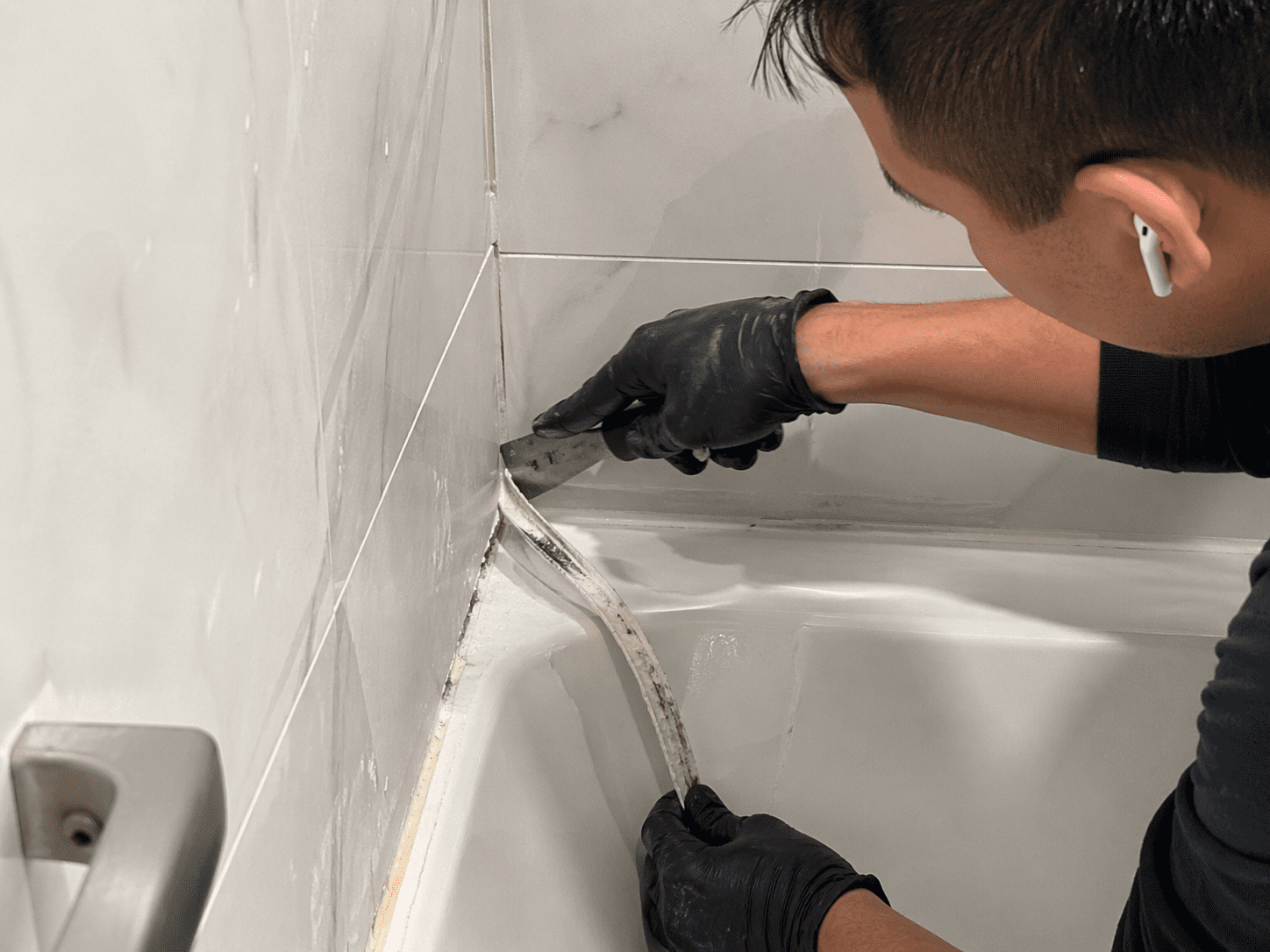 Removing old silicone caulking from bathroom shower during professional service in Toronto